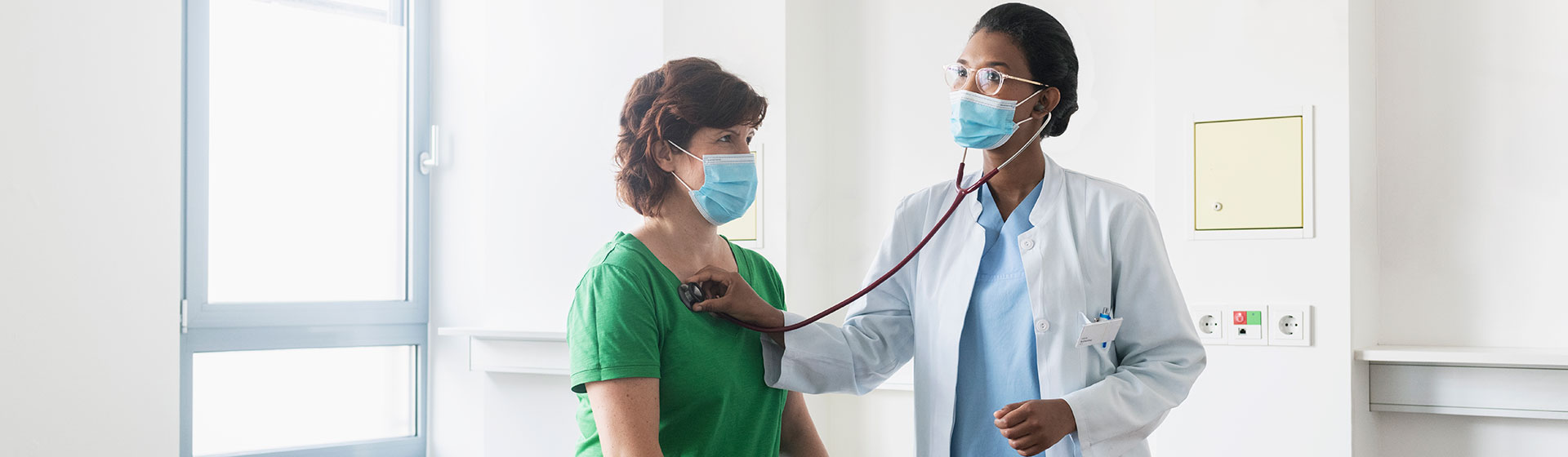 Masked female doctor checking patient's heart