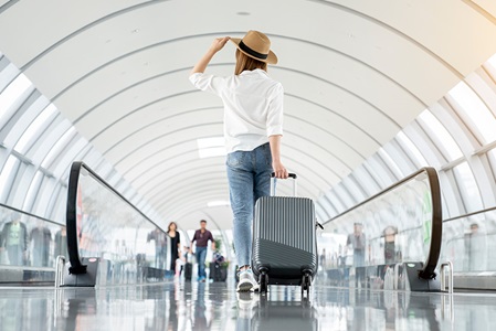 A woman walk through an airport with a suitcase in tow.
