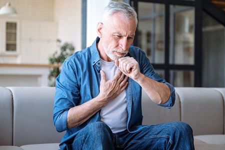 A man coughs while sitting on the couch.