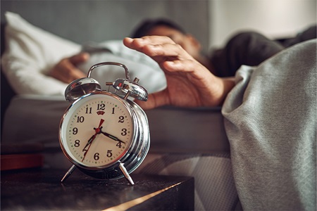 A man reaches for his alarm clock.