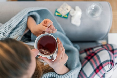 A woman drinks a cup of tea on the couch.