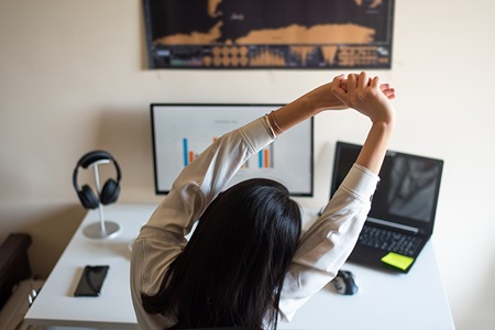 A woman stretches in front of her computer.