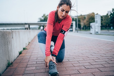 A woman tends to her ankle during a jog.